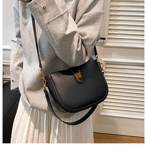 Close-up of black matte leather saddle bag with gold metal buckle and adjustable strap