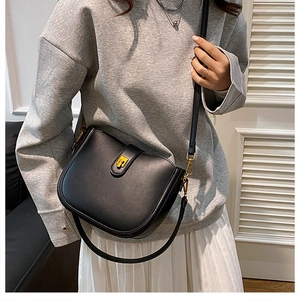 Model wearing a black saddle bag with gold buckle and adjustable leather shoulder strap