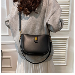 Detail view of a black leather saddle bag with gold buckle worn by a model in casual style