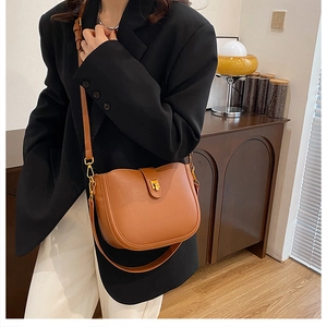 Detail of a brown leather saddle bag with gold metal buckle on a model wearing black blazer