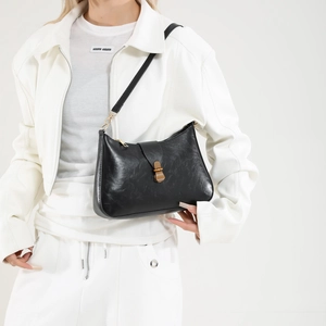 Minimalist black leather underarm bag with gold buckle on a model in sporty white outfit