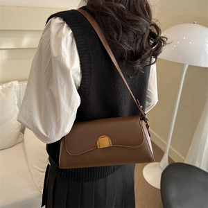 Sac baguette rétro marron foncé avec boucle dorée porté à l'épaule par un mannequin