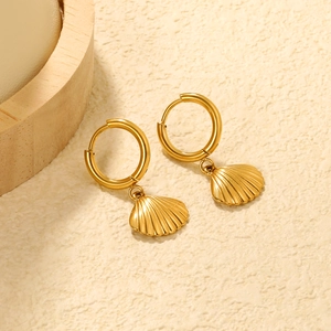 Detail of 18K gold-plated shell drop hoop earrings with textured finish on beige surface