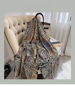 Détail d'une écharpe en satin de soie à motif cachemire gris sur un canapé beige