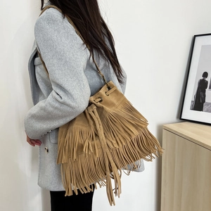 Bohemian suede tassel bucket bag with drawstring closure in camel brown worn as crossbody