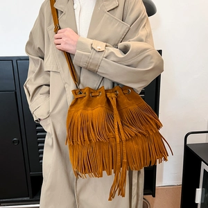 Caramel brown fringe bucket bag in suede finish with drawstring and crossbody strap