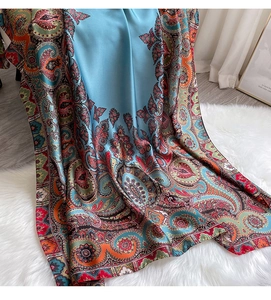 Détail d'une écharpe en soie bleu ciel avec motif paisley et fini satiné sur tapis blanc