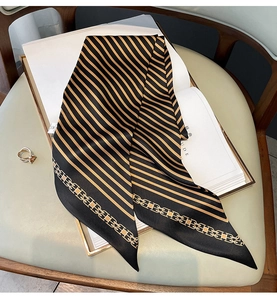 Gros plan d'un foulard Twilly en soie à rayures noir et or avec motifs de chaînes
