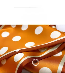 Macro detail of the smooth orange silk-like fabric with elegant white polka dots