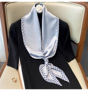 Detailed view of light blue silk scarf with houndstooth pattern tied on a dark outfit