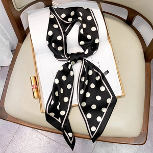 Elegant polka dot skinny silk scarf tied in a bow on a magazine for stylish hair or bag