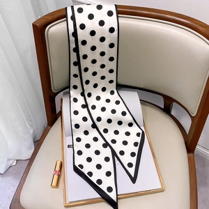 Close-up of a white polka dot skinny silk scarf draped over a chair with lifestyle props