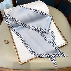 Detailed macro view of blue faux silk twilly scarf with geometric patterns on a white book