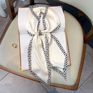 Elegant off-white satin silk scarf with black houndstooth pattern tied in a bow on a book
