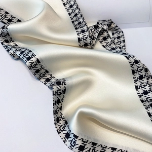 Close-up of ivory satin scarf showing smooth texture and geometric patterned border