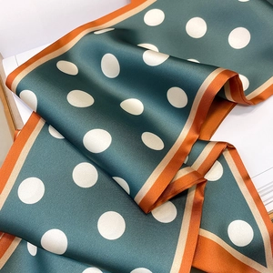 Detailed view of polka dot silk scarf in dark green with vibrant orange contrast borders