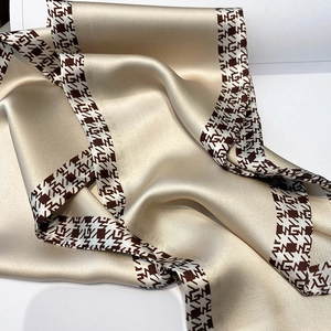 Detail of champagne gold satin scarf with houndstooth and letter G pattern ribbon trim