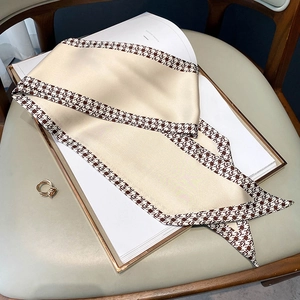 Detail of champagne silk-like scarf with brown geometric edges on a minimalist book