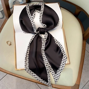 Elegant black silk scarf with houndstooth edge tied on a book and leather background