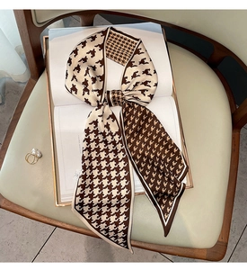 Close-up of houndstooth silk scarf tied in a bow on a white book for fashion styling