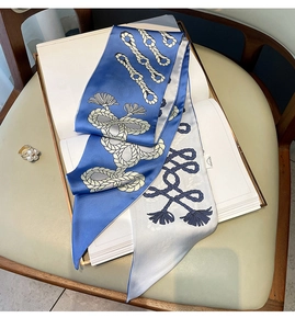 Détail d'un foulard en soie à motif corde nautique sur des livres avec accessoire perle