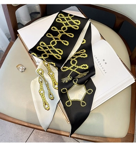 Détail d'un foulard en soie avec motif chaîne jaune sur magazine et fond en cuir