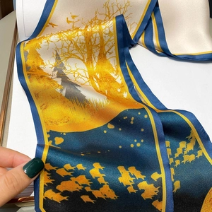 Detailed view of blue silk scarf texture featuring yellow artistic tree and bird patterns