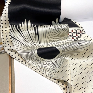 Close-up of black and white silk scarf with daisy patterns and polka dots on satin