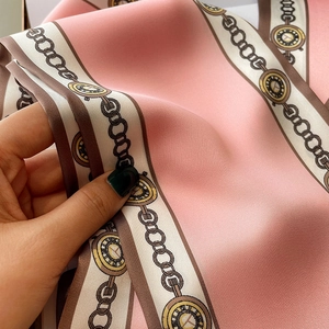Detail eines rosa Seidenschals mit Vintage-Uhrenmuster und goldenem Kettendruck
