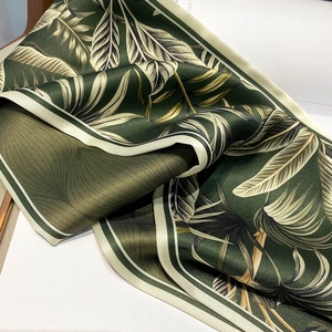 Detailed close-up of dark green tropical leaf print satin scarf with smooth silk texture