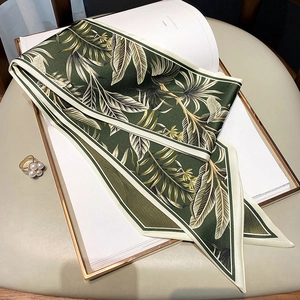 Close-up of a green palm leaf printed silk twilly scarf with elegant pearl ring accessory