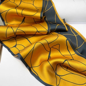 Dettaglio di un foulard in seta a doppia faccia con motivi geometrici gialli e grigi morbidi