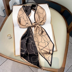Foulard twilly in seta champagne e nero con linee geometriche annodato su un libro