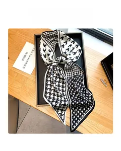 Détail d'un foulard en soie à motif pied-de-poule noir et blanc noué sur un plateau bois