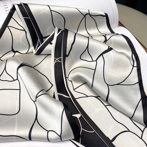 Vista dettagliata di un foulard in seta con linee nere geometriche e trama satinata lucida