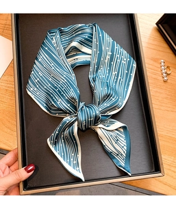 Détail d'un foulard en soie à rayures bleues noué en nœud sur un plateau noir avec perles