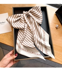 Détail d'un foulard en soie rayé noué en boucle avec imprimé chaîne sur satin de luxe