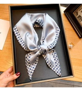 Détail d'un foulard étroit en soie bleu clair avec motifs géométriques sur plateau