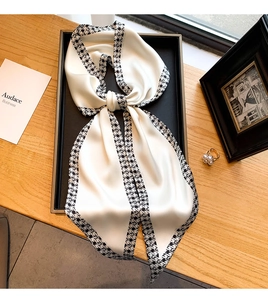 Détail d'un foulard étroit en soie satinée avec motif pied-de-poule noir sur fond beige