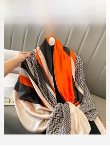 Detail of satin silk scarf with orange and black geometric patterns on a grey sofa