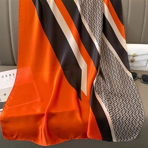 Detail view of large faux silk scarf with orange color block and geometric patterns