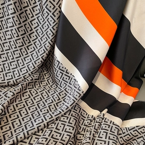 Detail of silk scarf showing orange stripes and black geometric patterns with soft luster