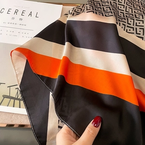 Detail of silk-satin scarf texture featuring orange and black geometric Greek patterns