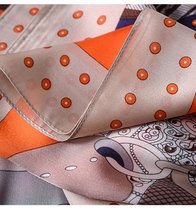Detailed view of silk scarf with orange and beige patterns and elegant pearl illustrations