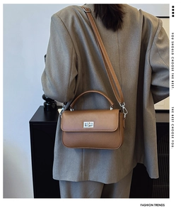 Detail of caramel brown leather crossbody bag with silver lock on grey blazer model