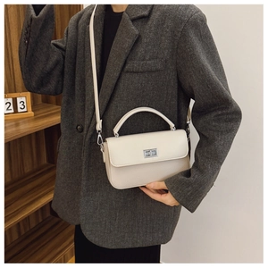 Detail of cream crossbody bag with silver twist lock on model in grey blazer