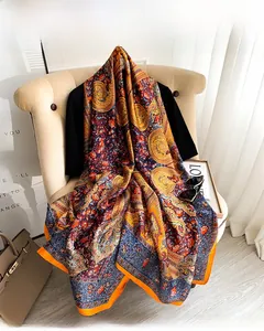 Detail view of retro paisley floral silk scarf with vibrant orange border on sofa