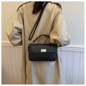 Black litchi leather bag with metal turn-lock on a model wearing a khaki trench coat