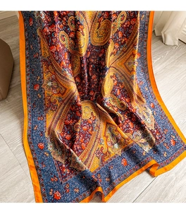 Detail of floral paisley print on smooth silk shawl with bright orange hem on wood