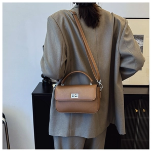 Back view of brown leather crossbody bag with silver lock worn by model in a chic setting